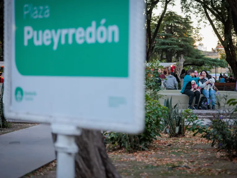 Boulevard Gálvez en Santa Fe Capital, con un cartel que indica Plaza Pueyrredón y personas descansando en el paseo junto a sus mascotas.
