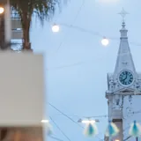Torre campanario blanca de la Basílica del Carmen en Santa Fe con su gran reloj circular azul, recortada contra el cielo y rodeada de guirnaldas de luces desenfocadas.