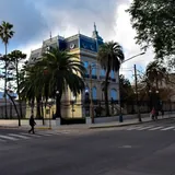 Fachada de la Casa de la Cultura en Santa Fe, una mansión histórica de estilo francés con mansardas azules, rejas perimetrales y palmeras frente a la calle