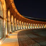 Vista nocturna de la fachada curva e iluminada de La Redonda, Arte y Vida Cotidiana, destacando sus grandes ventanales con arcos de ladrillo visto.