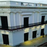 Vista aérea angular de la Fachada de la Casa del Brigadier Estanislao López en Santa Fe, un edificio histórico de dos pisos pintado de blanco e iluminado por luces empotradas al anochecer.