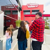 Una guía turística recibe a un grupo de visitantes y niños frente a las instalaciones modernas del local de alfajores Merengo en Santa Fe.