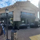 Fachada del Mercado Norte en Santa Fe, un edificio histórico de estilo clásico ubicado en la esquina de Santiago del Estero. La estructura alberga locales comerciales como barberías y cafés, con mesas